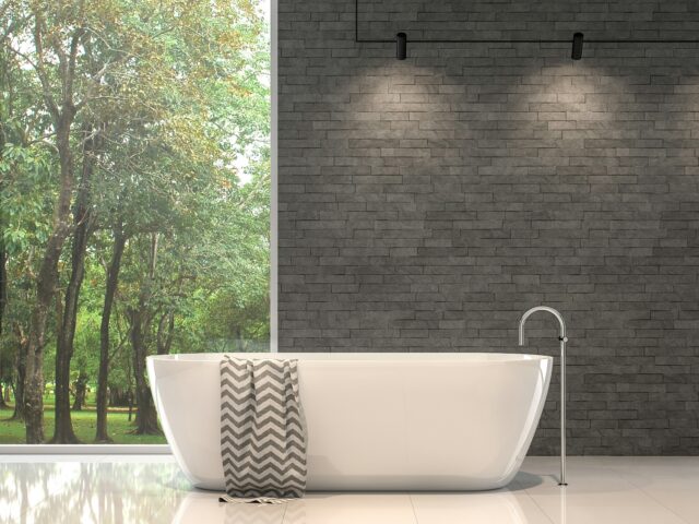 Open-plan bathroom with a freestanding tub, large window overlooking a green forest, and modern lighting.