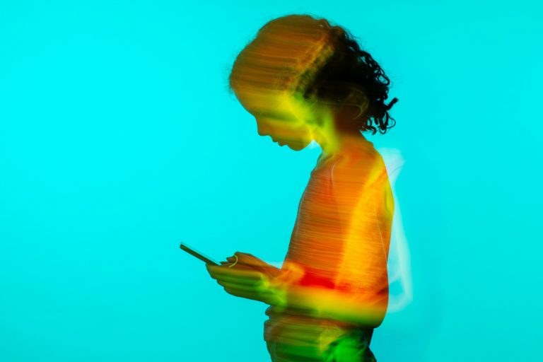 Silhouette of a young person engrossed in using a smartphone, depicted with vibrant light trails on a blue background, symbolizing digital connectivity and the dynamic impact of social media.