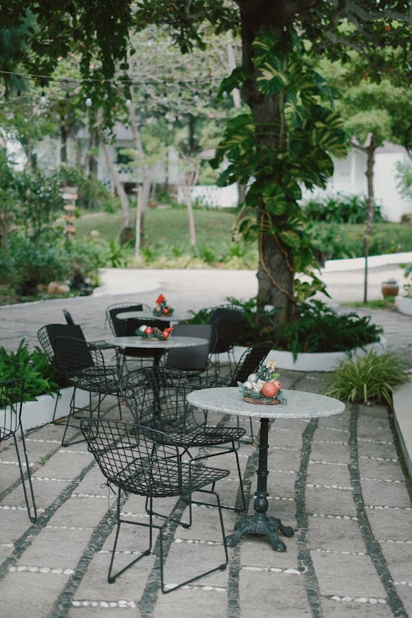 A serene garden patio with wire chairs and tables in a lush outdoor setting.