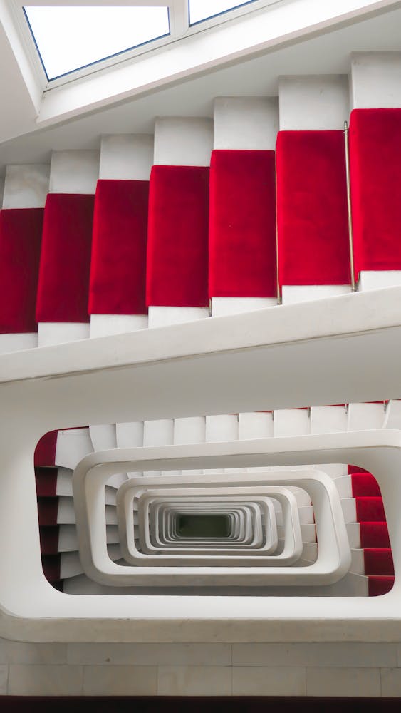 A striking top-down view of a red carpeted spiral staircase indoors in Lyon, France.