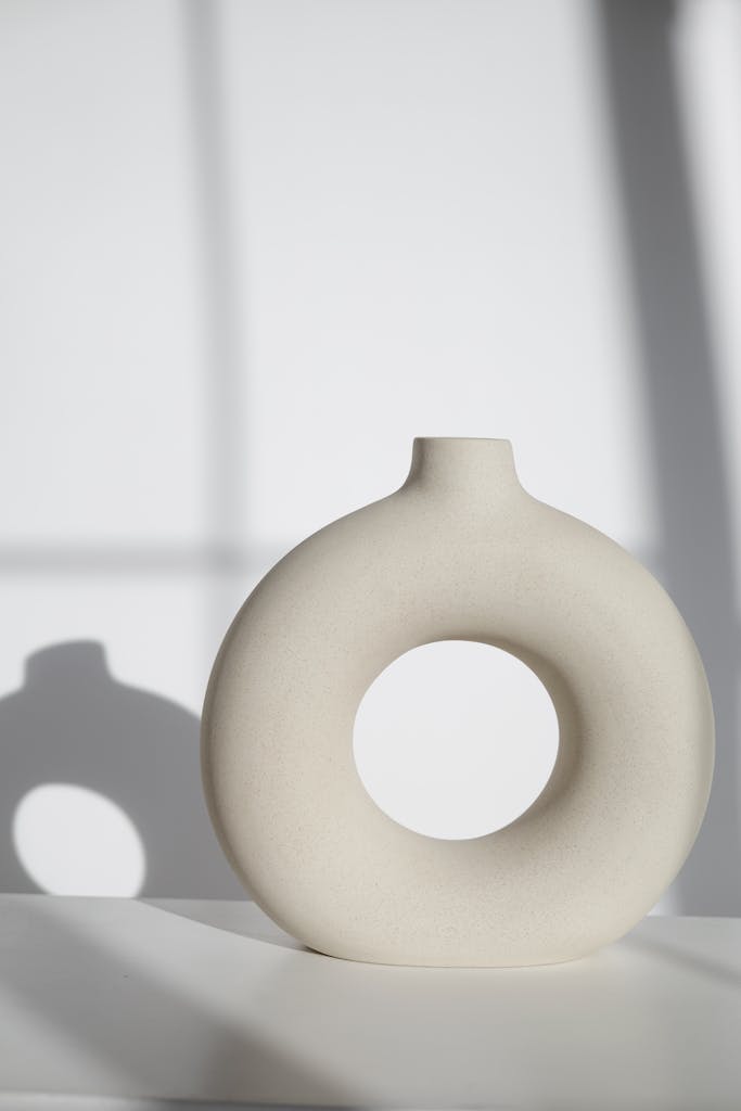 Elegant circular ceramic vase casting gentle shadows indoors, a simple and stylish decor piece.