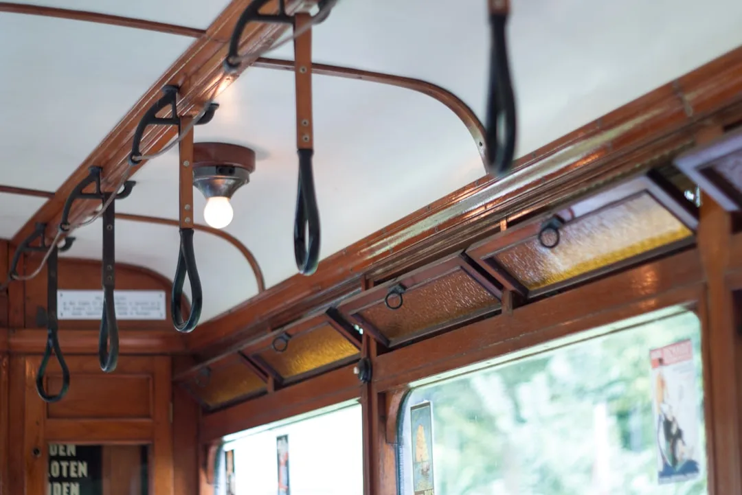 Warm amber light glowing inside vintage wooden tram with hanging leather straps and ornate wood paneling