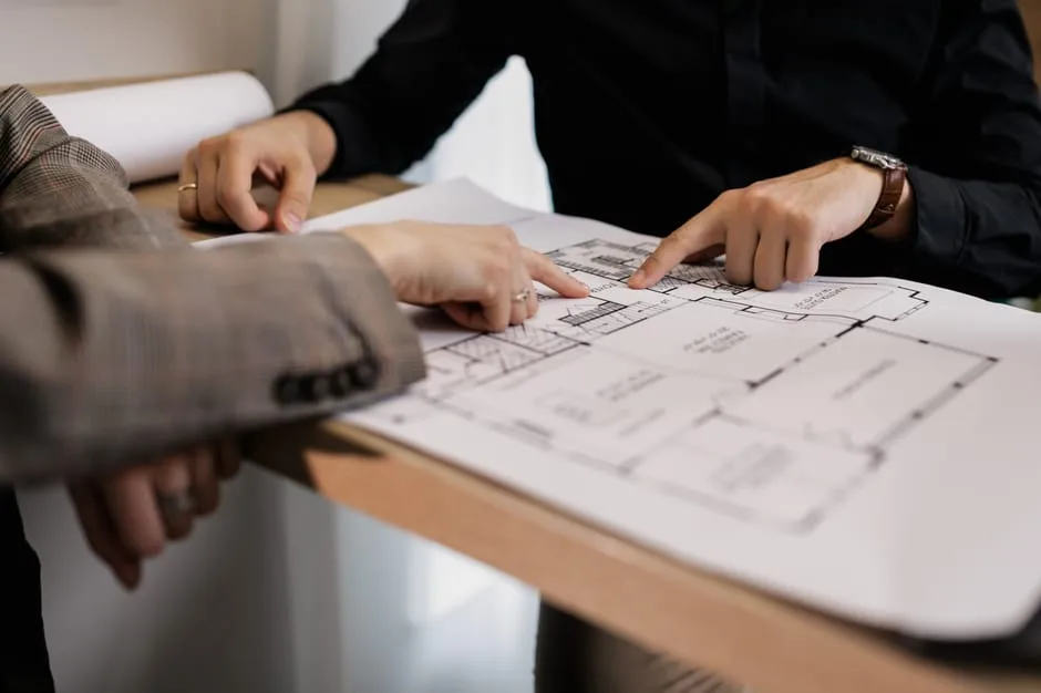 Two architects reviewing architectural floor plan blueprints on a table, pointing at layout details