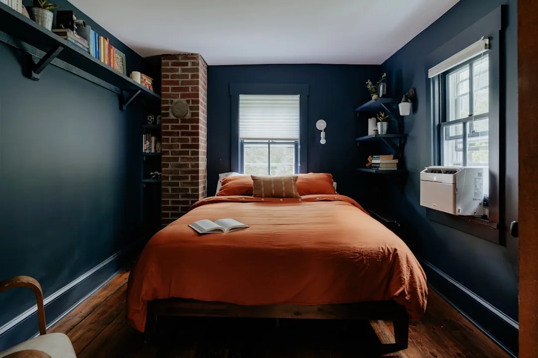 DIY navy blue bedroom accent wall with exposed brick column and rust orange bedding on wood platform bed