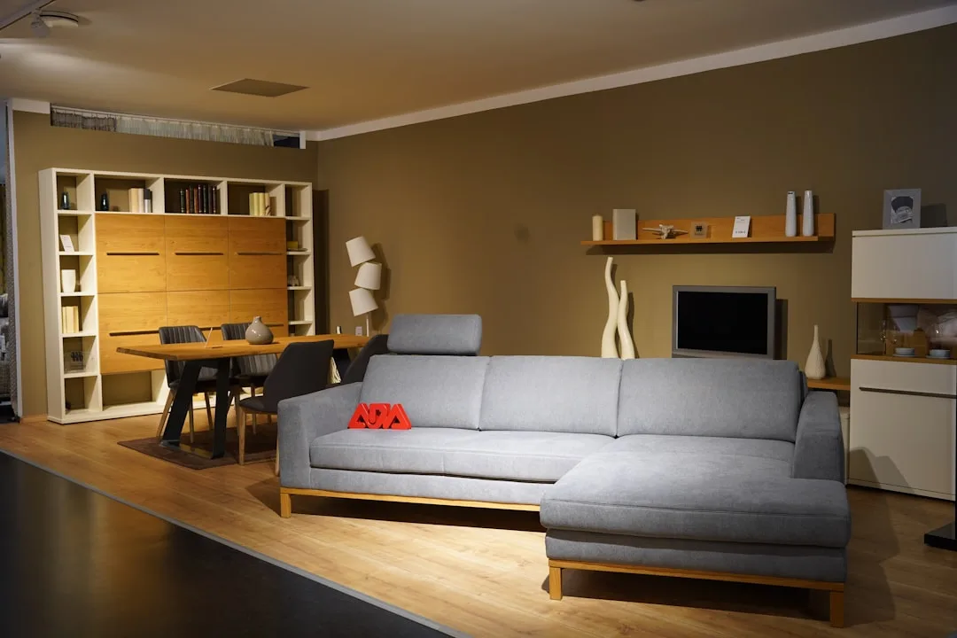 Modern living room showroom with gray sectional sofa, wooden shelving unit, and minimalist holiday display decor