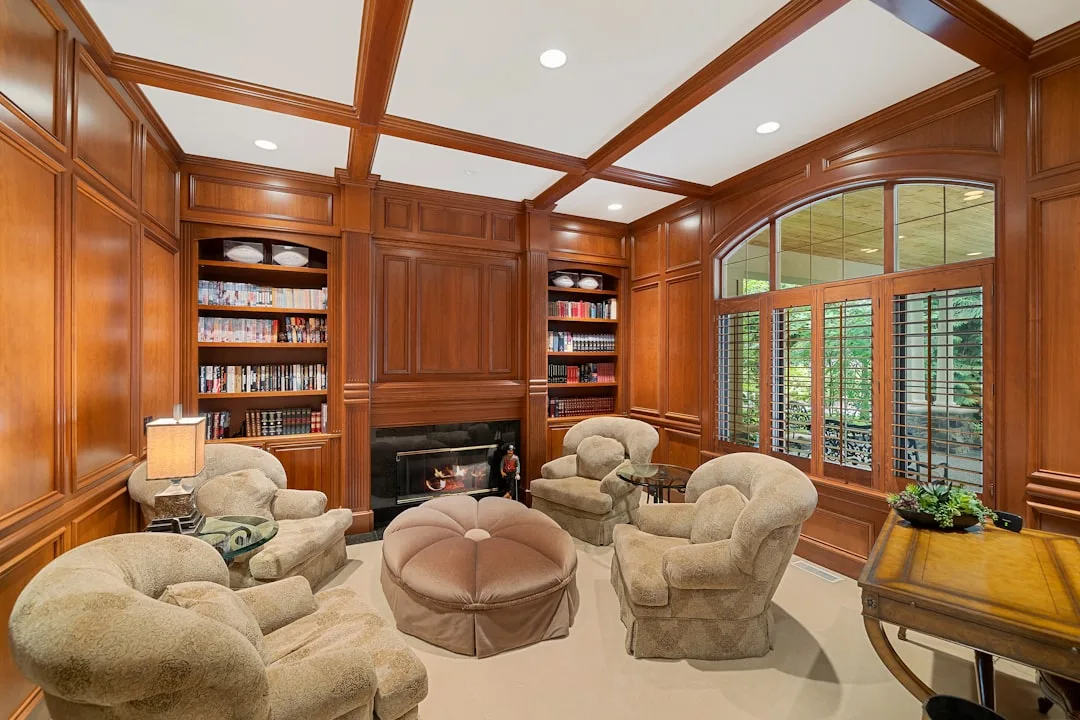 Built-in wood bookshelves flanking a fireplace in a luxury home library study with coffered ceiling