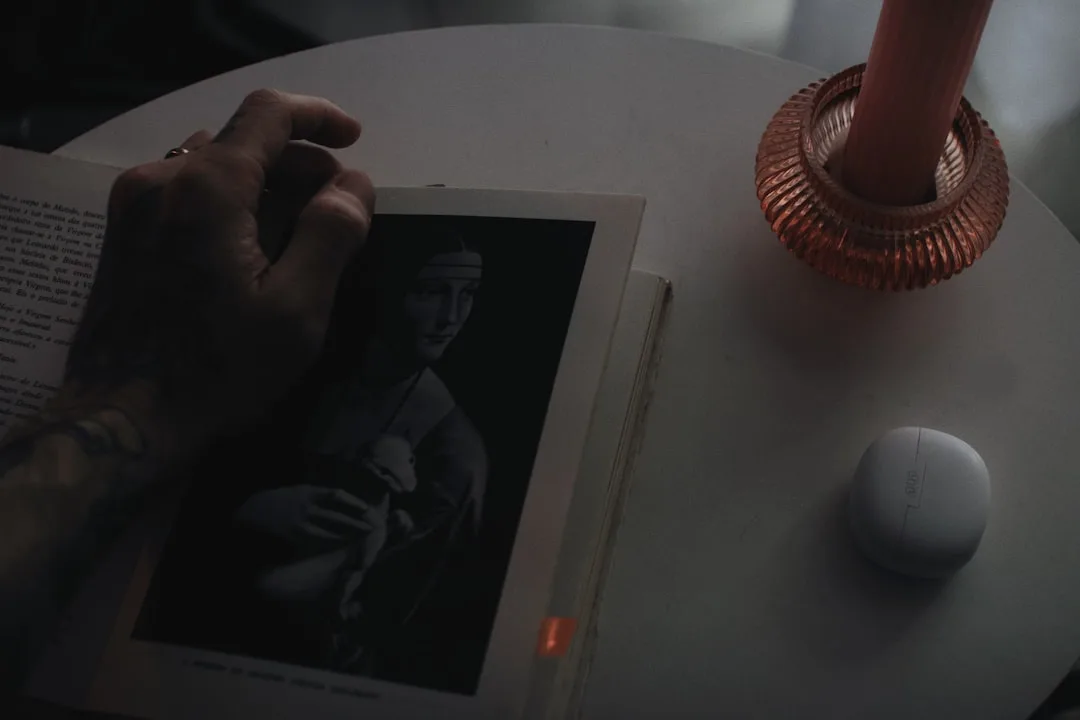 Hand holding art book with candle and small speaker on white table creating cozy multi-sensory atmosphere