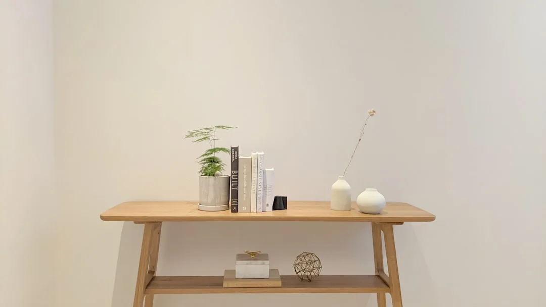 Slim wooden console table styled with books, plant, and white ceramic vases as minimalist bedside alternative