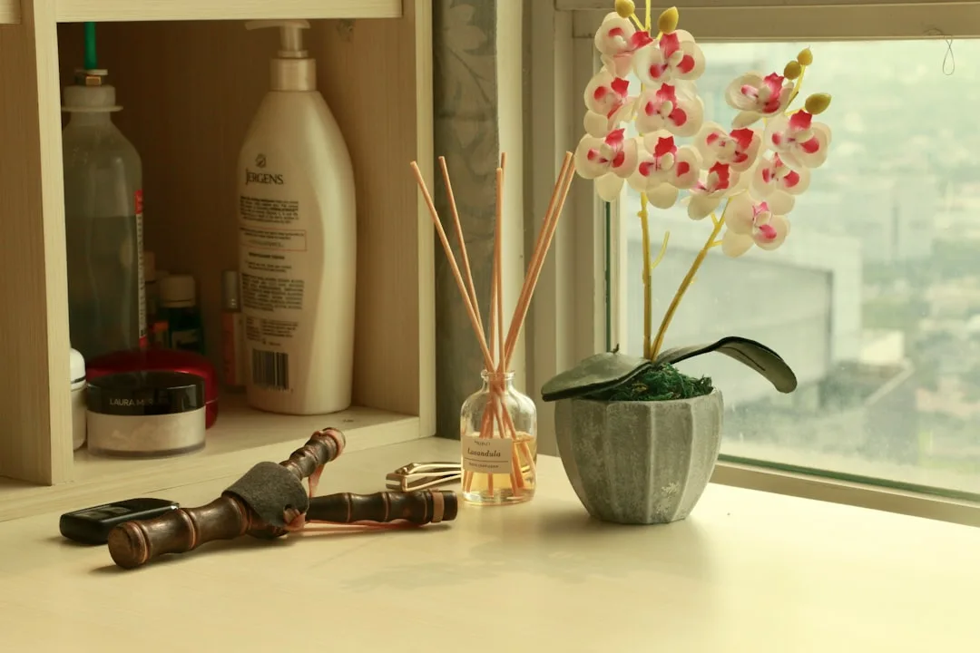 Reed diffuser with lavender scent sticks beside white orchid plant on windowsill with warm natural lighting
