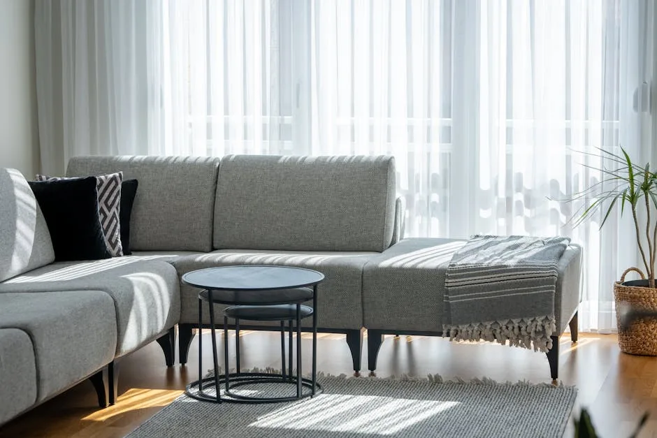 Gray L-shaped sectional sofa in modern living room with natural light, nesting tables, and area rug illustrating proper 