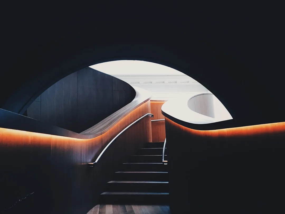 Architectural staircase with warm LED strip lighting integrated into curved wooden handrails in modern interior design