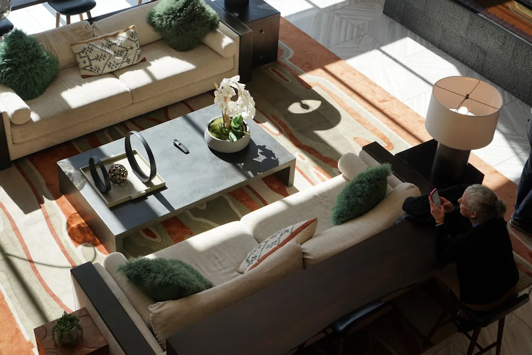 Overhead view of living room with large patterned rug anchoring cream sofas, coffee table, and green accent pillows