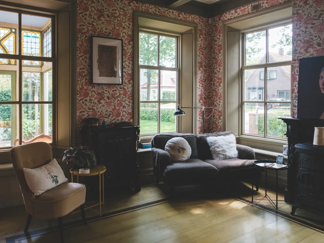 Victorian living room with red floral wallpaper, dark sofa, stained glass windows and hardwood floors