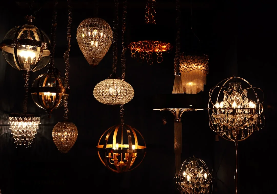 Collection of warm-glowing crystal and metal chandeliers and pendant lights displayed against dark background