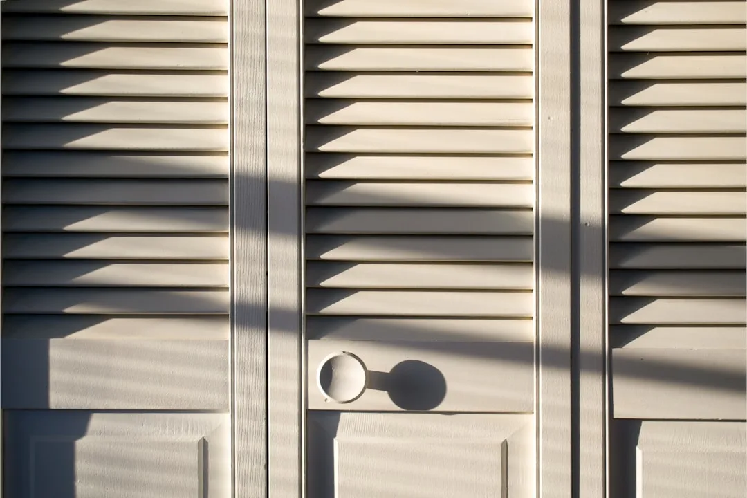 White louvered closet doors with round knob casting shadows in natural light showing door swing clearance area
