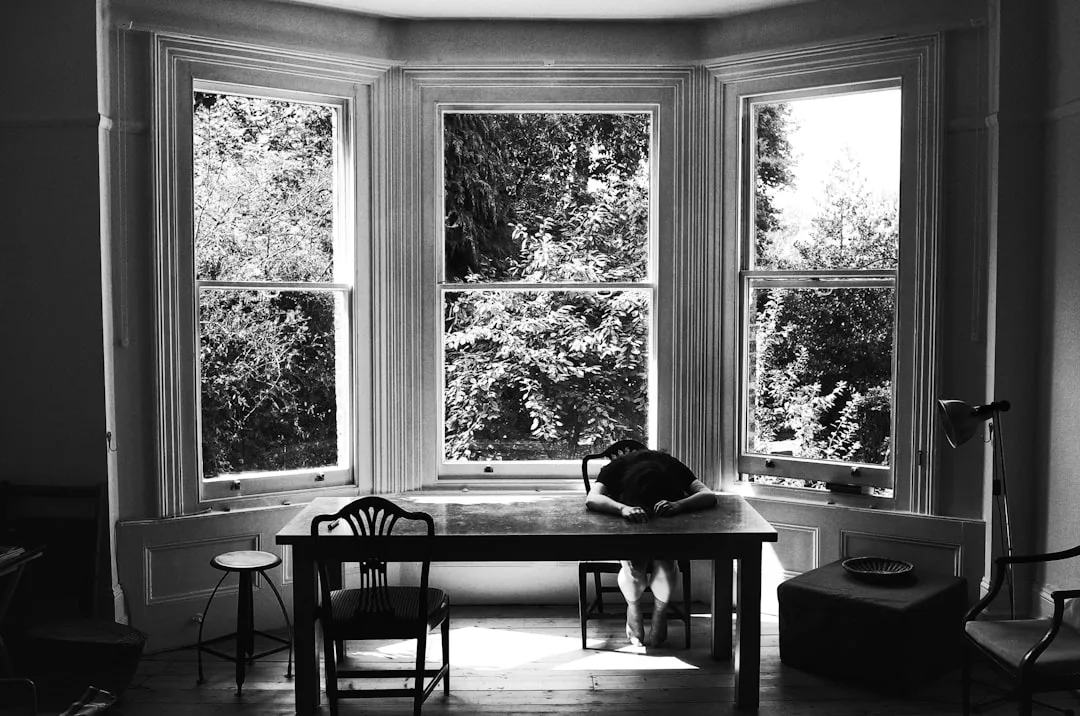 Black and white photo of a bay window with three panels flooding natural light onto a wooden desk in a home study
