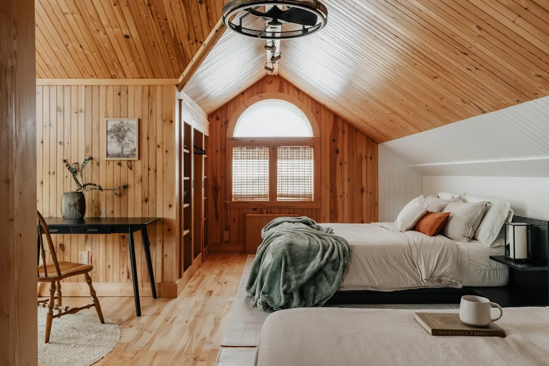Attic bedroom with slanted wood ceiling, knee wall storage, arched window, and cozy bed with green throw blanket