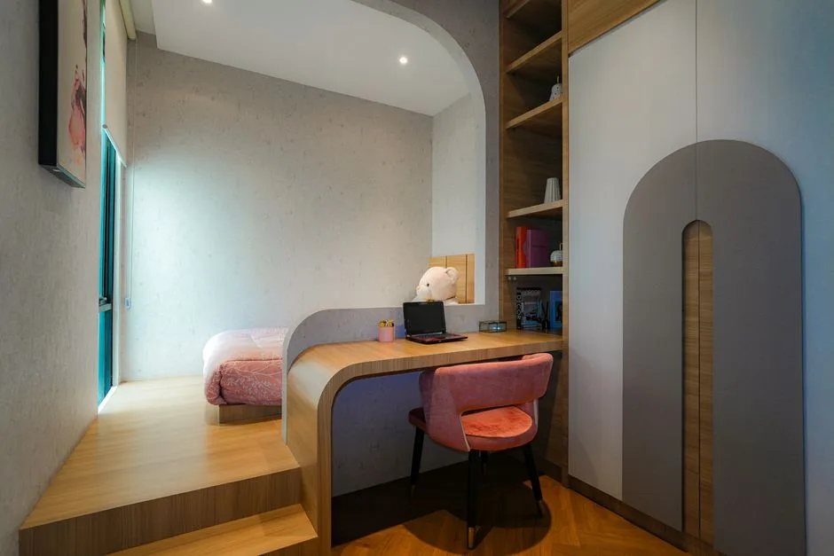 Built-in wooden desk integrated with raised platform bed in small bedroom with arched wardrobe and open shelving