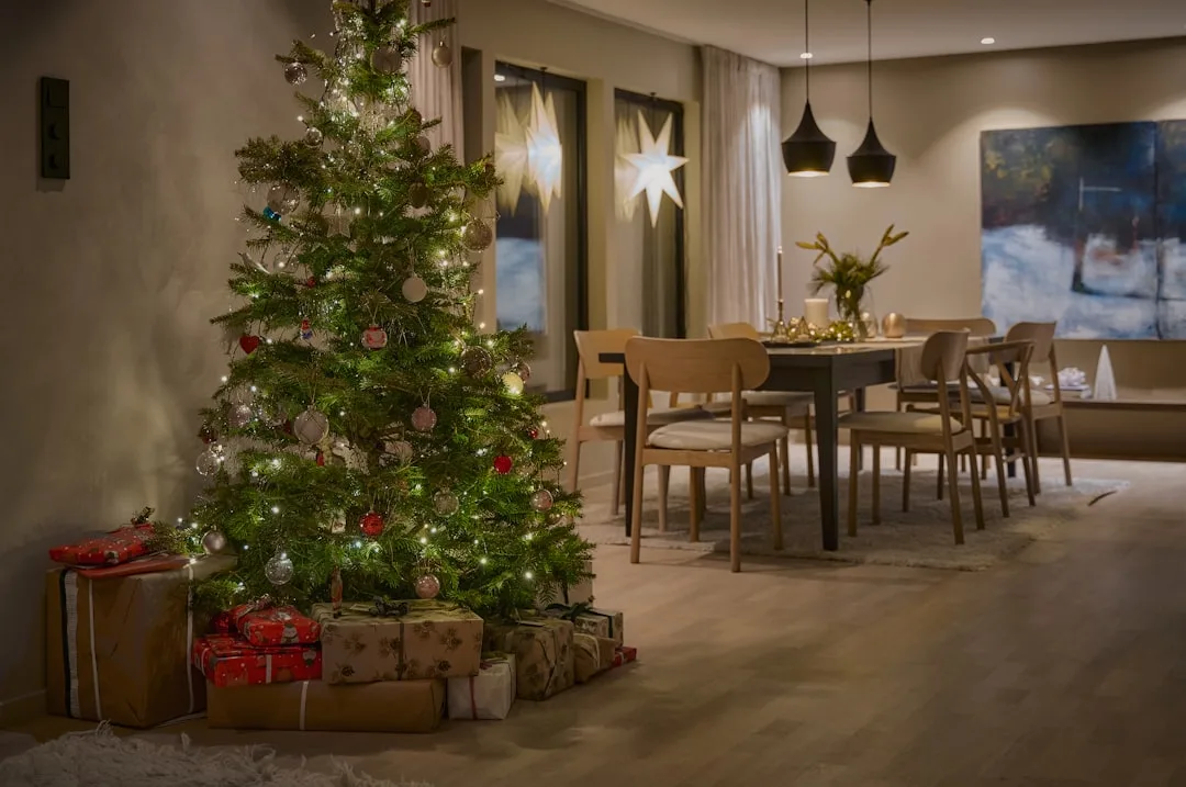 Christmas tree with fairy lights and wrapped gifts in a small modern apartment dining room with minimal Scandinavian dec