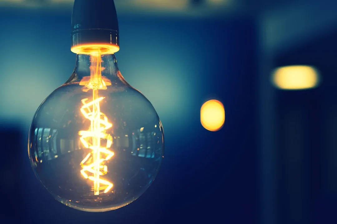 Glowing Edison filament bulb with spiral filament hanging against deep blue background