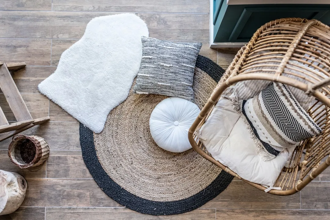 Layered natural jute round rug with sheepskin throw, woven cushions, and rattan chair on wood floor