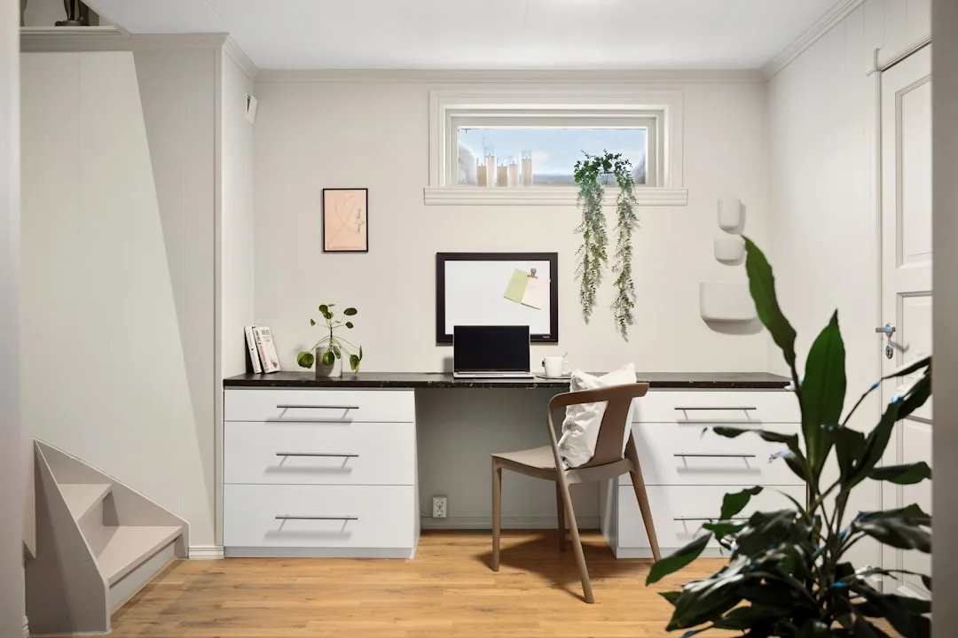 Built-in white desk with black countertop and drawer storage in a minimalist home office with wood floors