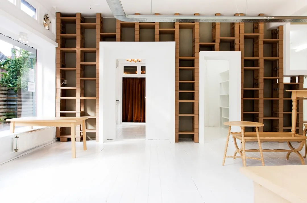 Floor-to-ceiling modular wooden bookcase built into white room with open shelving and white painted floors