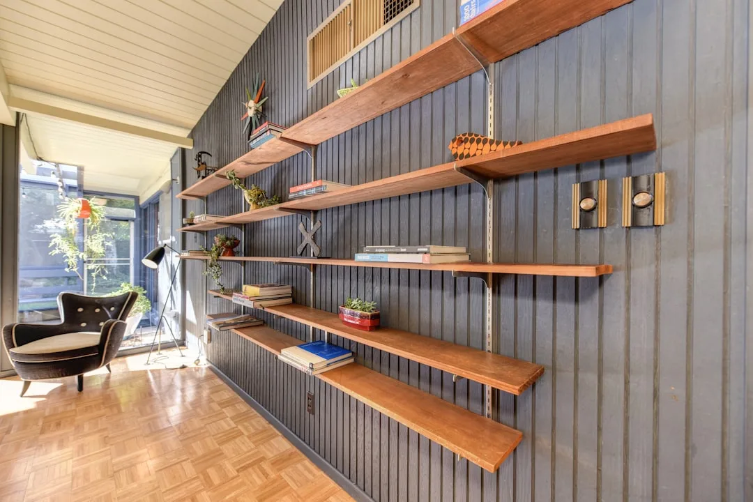 Mid-century modern wall-mounted floating wood shelves with books and plants in a small home office reading room