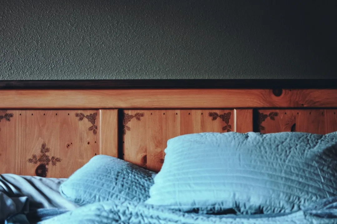 Wooden headboard with pine cone engravings and light blue pillows against a dark textured wall in a cozy bedroom