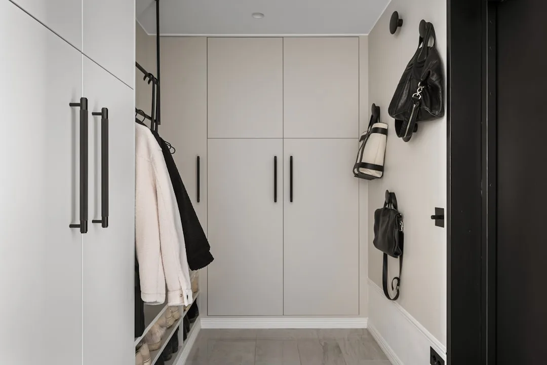 Modern walk-in wardrobe with beige built-in cabinets, black handles, and visible toe-kick base detail at floor level
