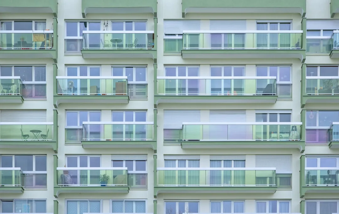 Apartment building facade with rows of glass balconies and large windows decorated with colorful panels and blinds