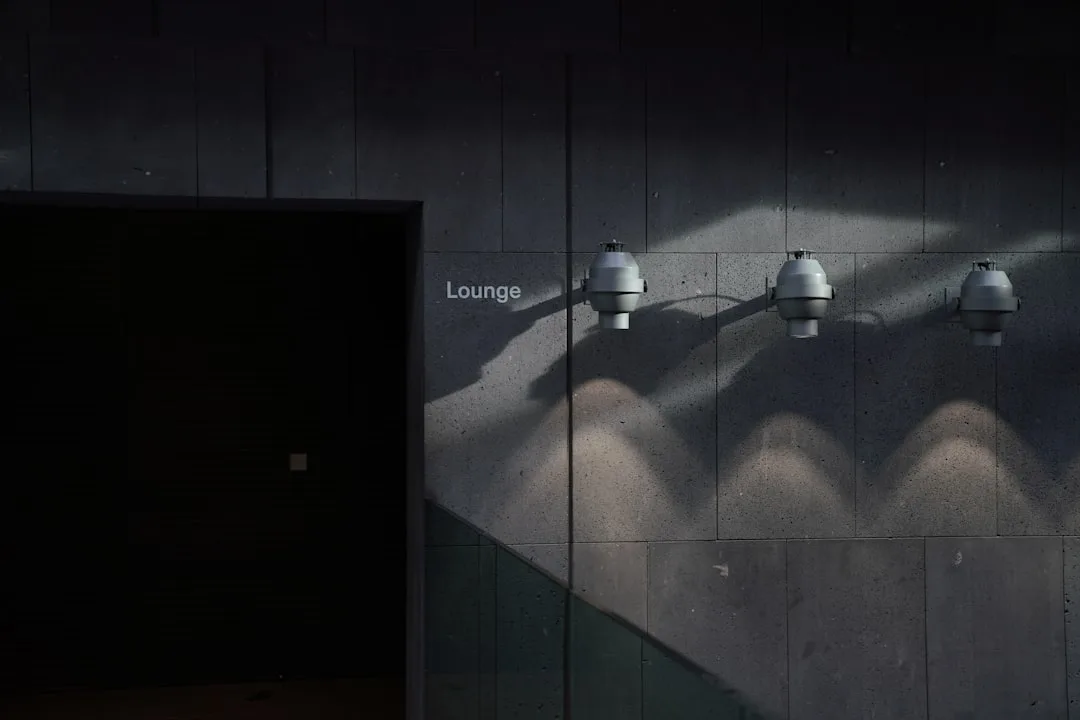 Industrial wall-mounted pendant lights casting dramatic shadows on concrete wall near lounge entrance