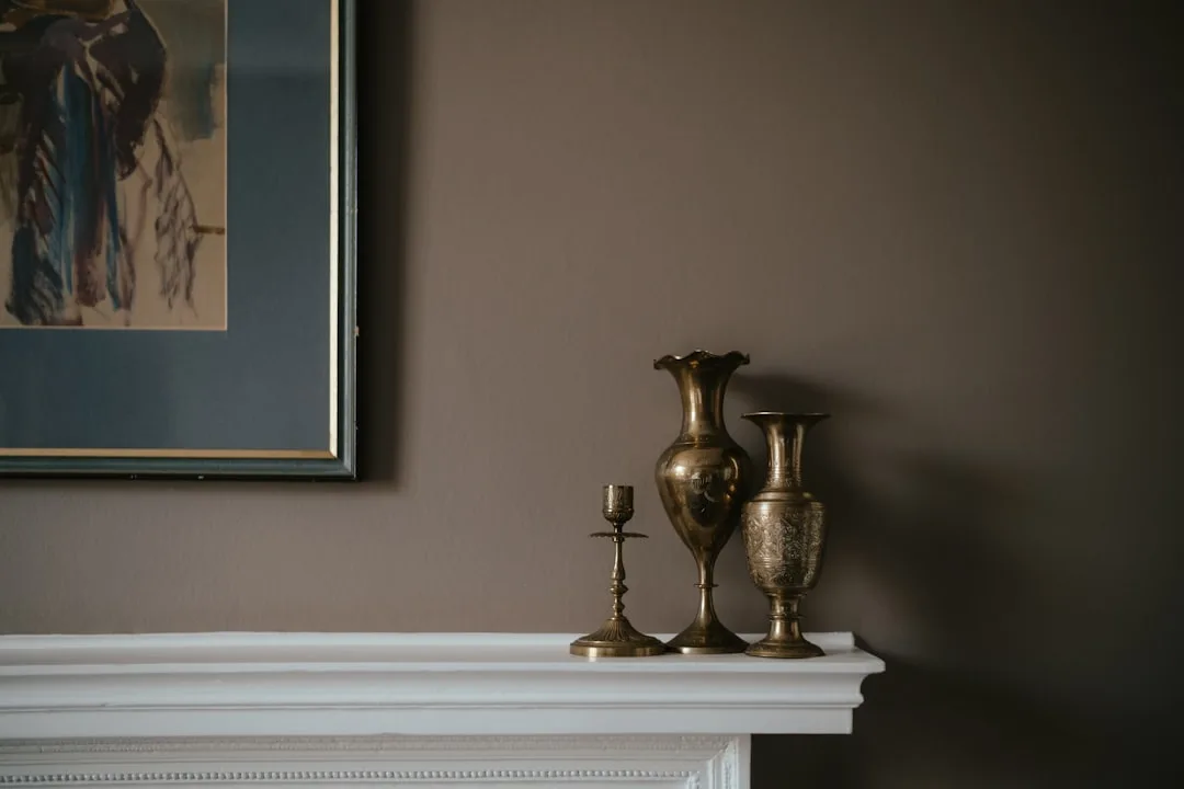 Three brass vases and candlestick arranged as a cohesive composition on a white fireplace mantel