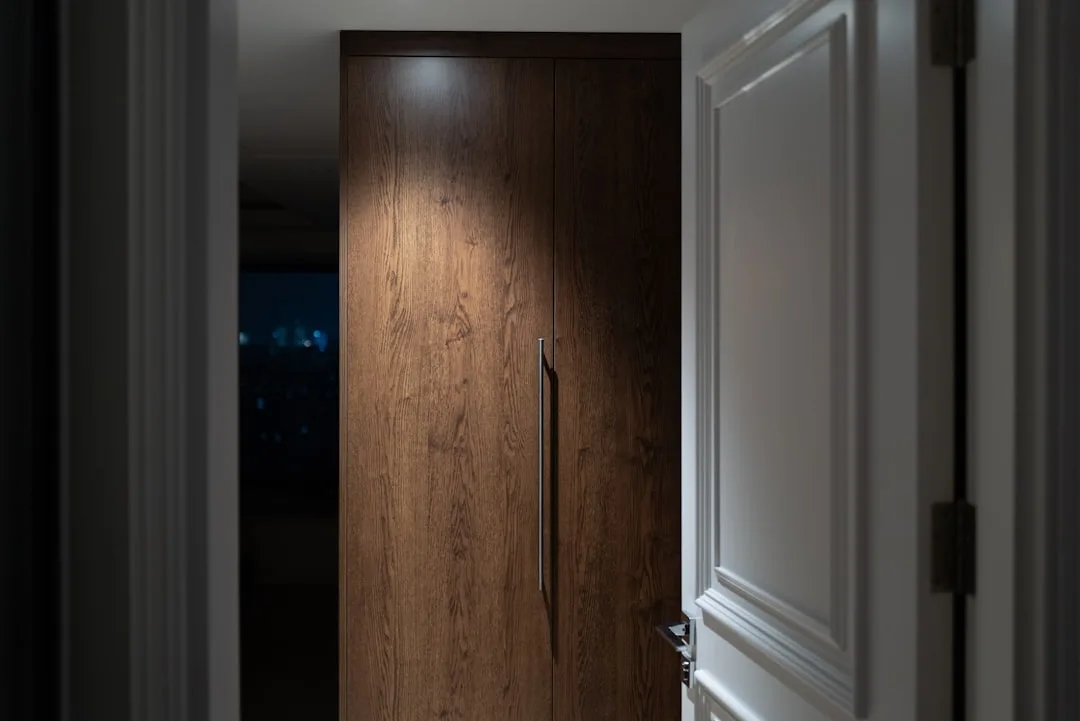 Dark wooden wardrobe doors visible behind an open white bedroom door creating a triangular dead zone space