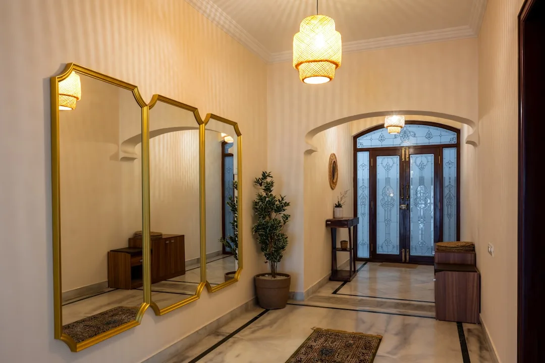 Large gold-framed triptych mirror in elegant entryway hallway reflecting light and space with pendant lamp