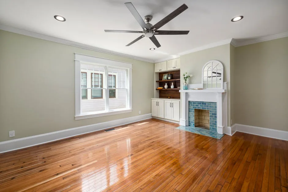 Empty living room with blue tile fireplace, white mantel, built-in shelves, and polished hardwood floors