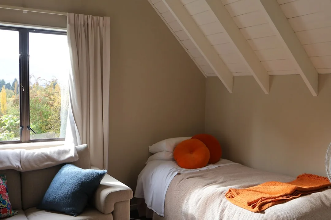Attic bedroom with orange round cushions, orange throw blanket, and neutral linen on single bed under sloped ceiling