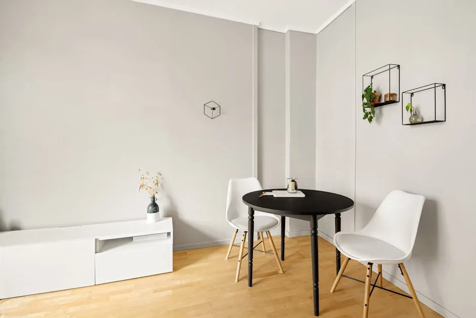 Minimalist small apartment dining area with monochromatic white walls, black round table, and white chairs on light wood