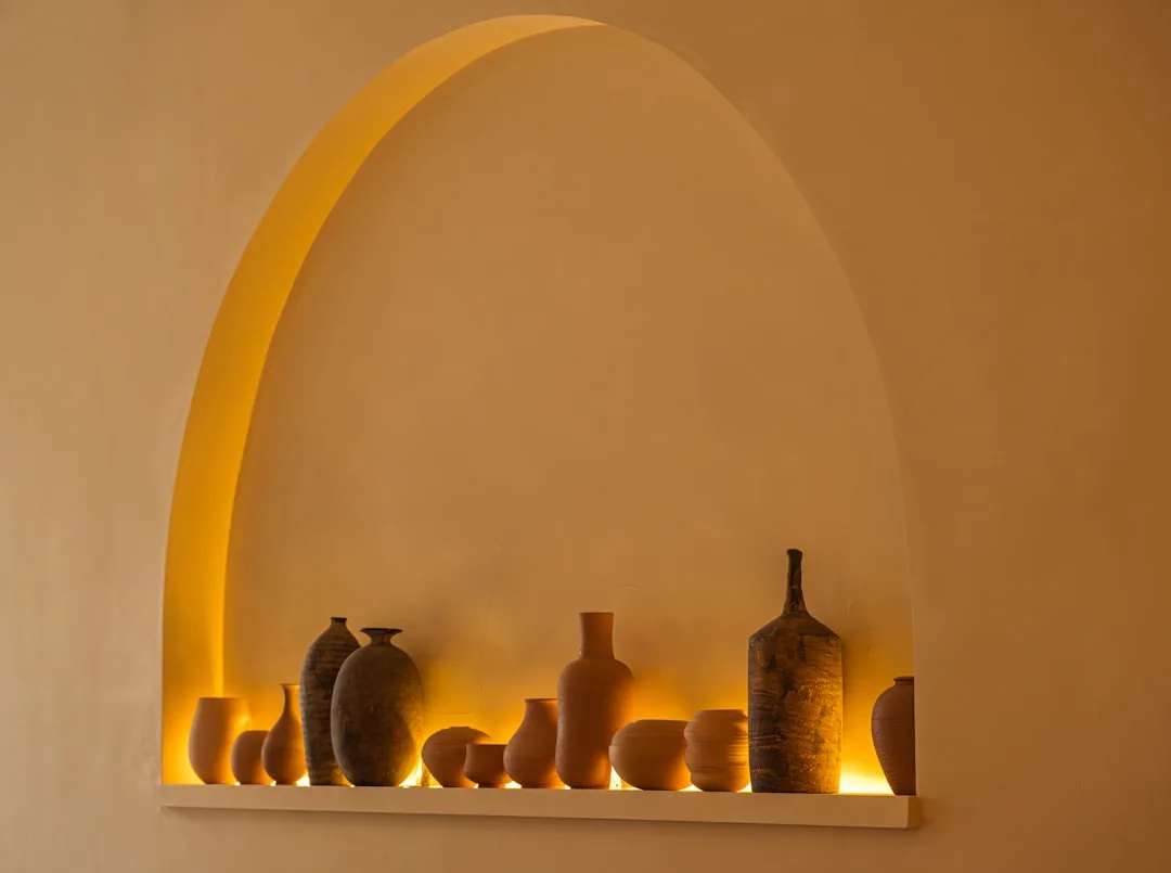 Arched recessed niche in wall displaying ceramic pottery collection with warm LED strip lighting underneath
