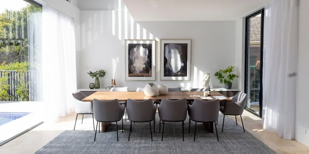 Modern dining room with large wooden table, gray upholstered chairs, abstract wall art and natural light for Christmas d