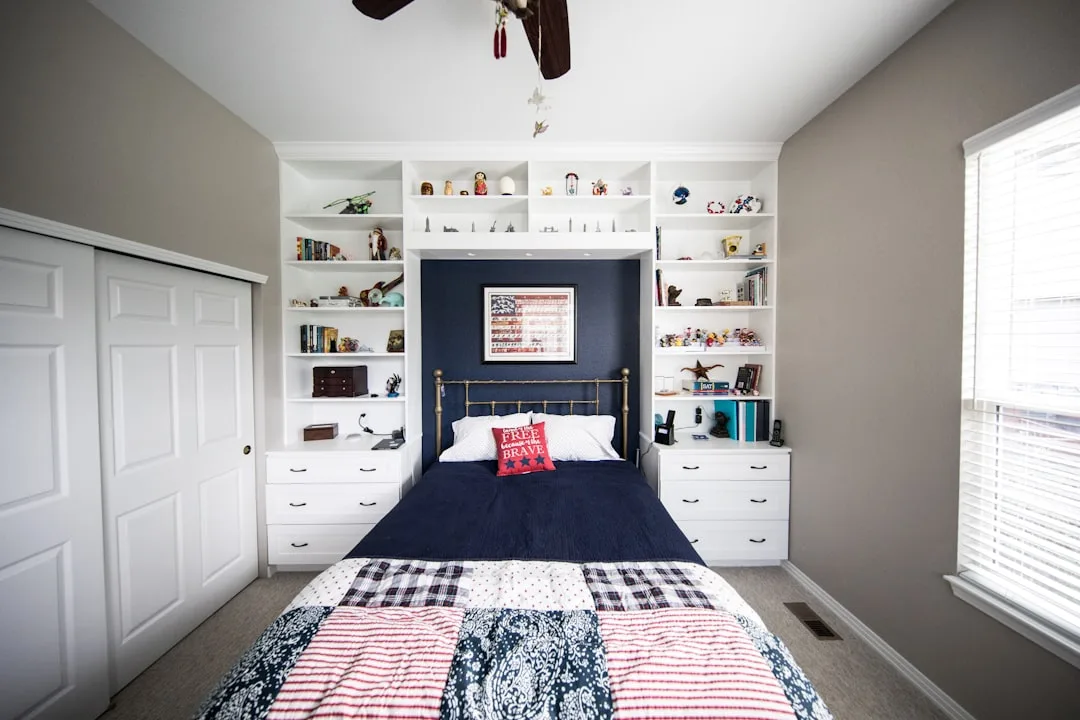 Built-in white shelving unit surrounding bed headboard with integrated storage drawers in a bedroom