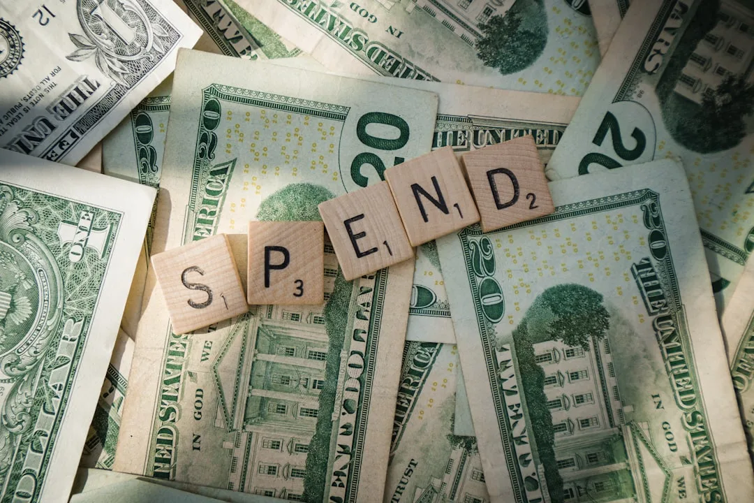 Scrabble tiles spelling SPEND placed on pile of US twenty dollar bills illustrating budget allocation framework
