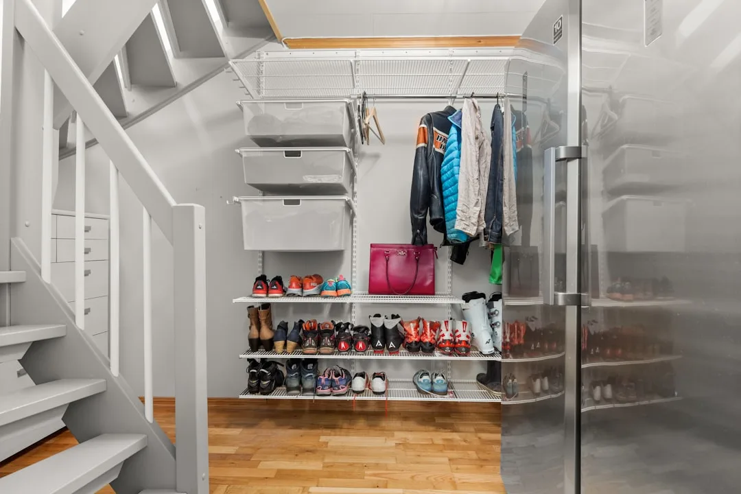 Organized walk-in closet under stairs with wire shelving, shoe racks, storage bins, and hanging jackets in small apartme