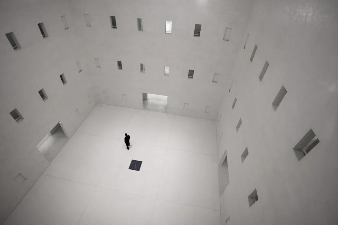 Lone figure standing in vast minimalist white architectural courtyard illustrating scale and empty space concept