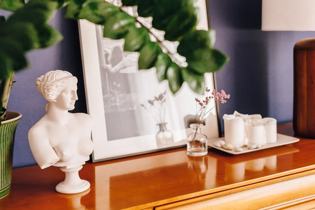 White Venus de Milo bust on mid-century modern wooden dresser with mirror, candles, and dried flowers for thrift store d
