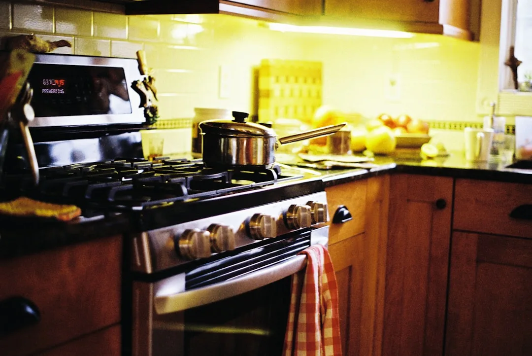Stainless steel gas range with pot on burner in warm kitchen with wood cabinets and under-cabinet lighting