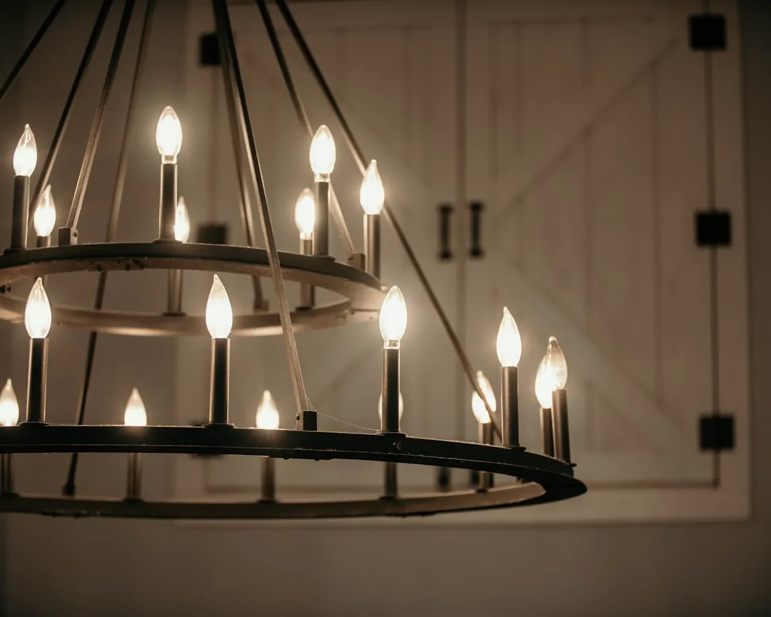 Two-tier farmhouse wagon wheel chandelier with candle-style bulbs hanging in front of white barn doors