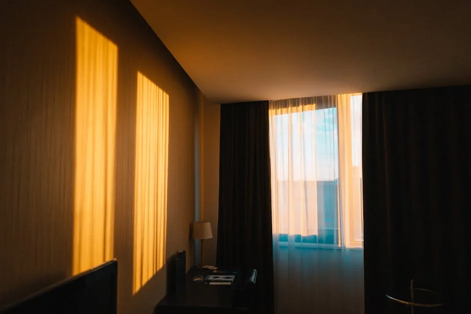 Hotel bedroom with layered curtains showing sheer and blackout drapes on floor-to-ceiling window at golden hour