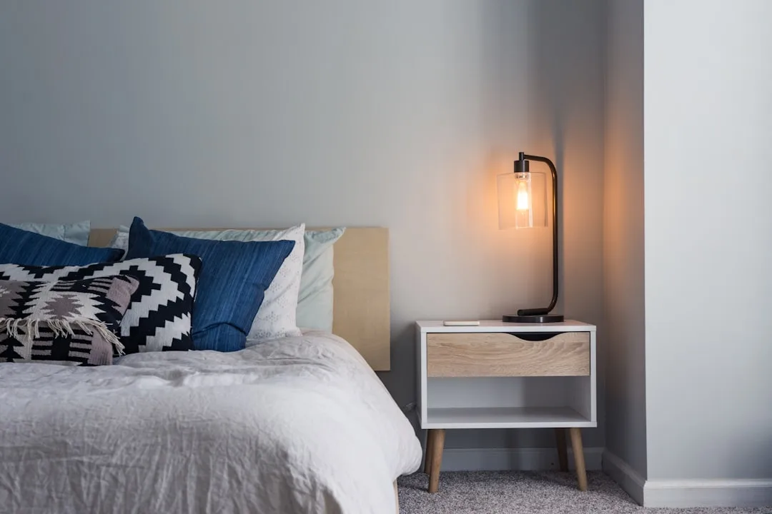 Warm Edison bulb bedside lamp on modern nightstand next to bed with blue and white pillows for sleep-friendly lighting