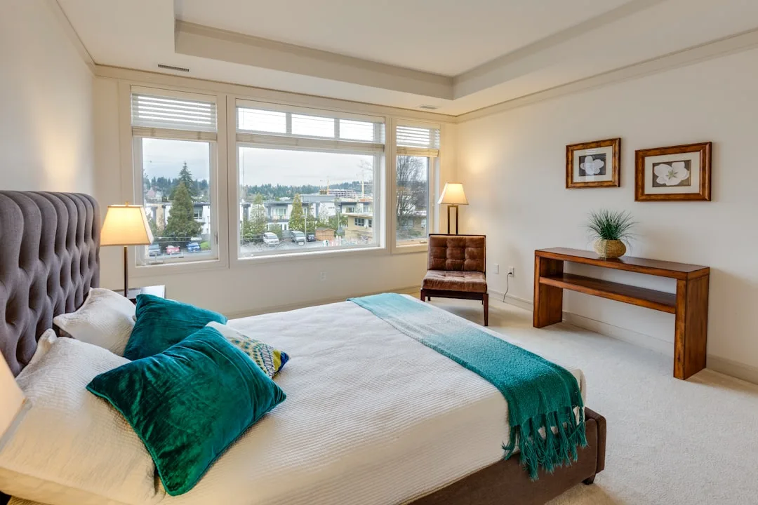King-size bedroom with tufted headboard, cream carpet, and teal accent throw showing ideal rug placement area